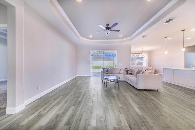 living room featuring ceiling fan with notable chandelier, light hardwood / wood-style flooring, and a tray ceiling