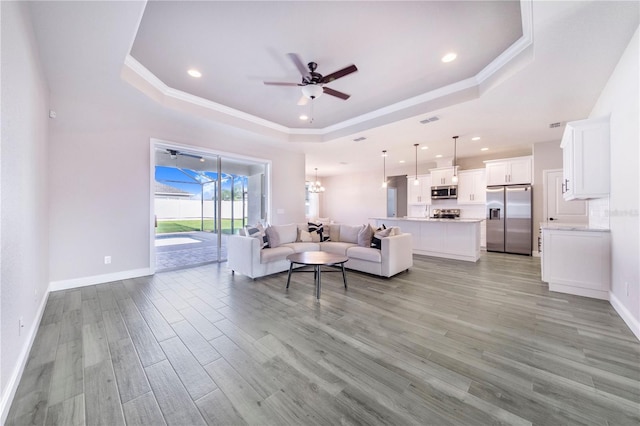 living room with a tray ceiling, light hardwood / wood-style floors, and ceiling fan with notable chandelier