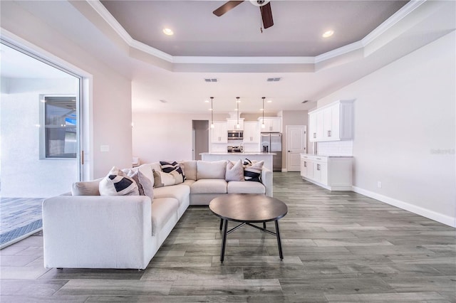 living room featuring ceiling fan, a raised ceiling, ornamental molding, and light wood-type flooring