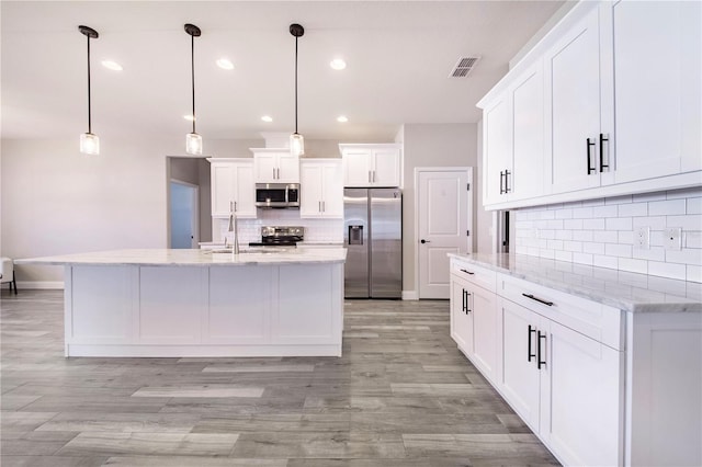 kitchen featuring stainless steel appliances, decorative light fixtures, white cabinetry, tasteful backsplash, and an island with sink