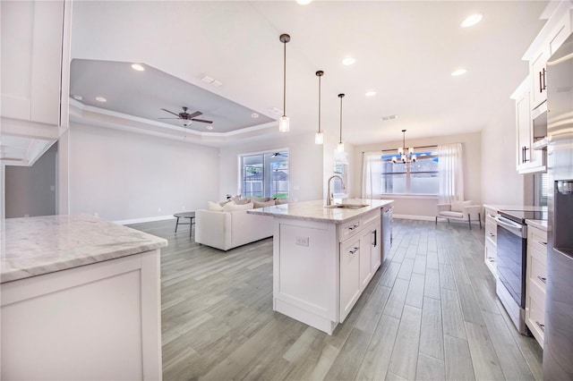 kitchen with appliances with stainless steel finishes, light hardwood / wood-style flooring, an island with sink, and a tray ceiling