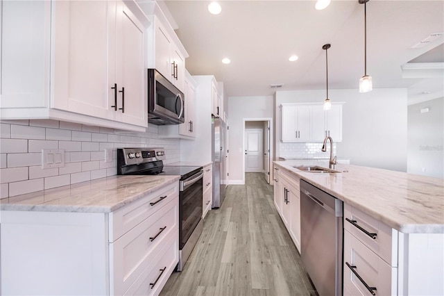 kitchen with decorative backsplash, white cabinets, appliances with stainless steel finishes, light hardwood / wood-style floors, and decorative light fixtures