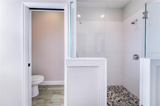 bathroom with toilet, wood-type flooring, and tiled shower