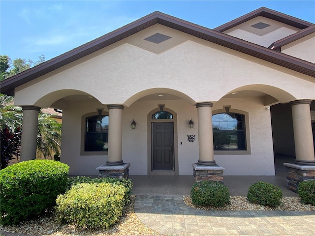 view of exterior entry with covered porch and stucco siding