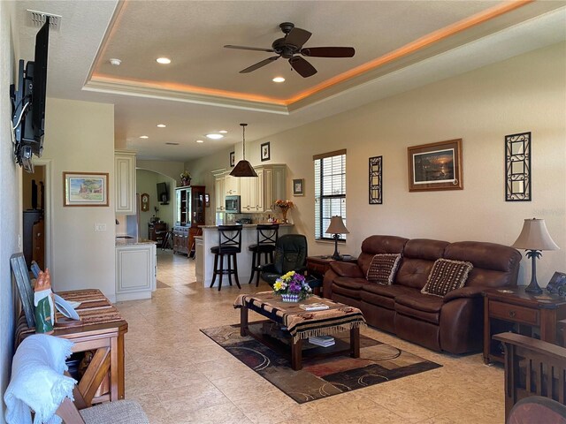 tiled living room featuring ceiling fan and a raised ceiling