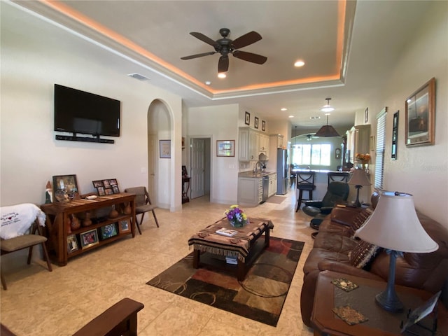 living area featuring arched walkways, recessed lighting, a raised ceiling, visible vents, and ceiling fan