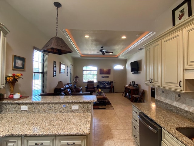 kitchen with dishwasher, light stone counters, open floor plan, cream cabinets, and a tray ceiling