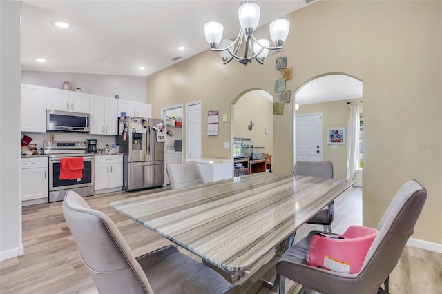 dining space featuring high vaulted ceiling, an inviting chandelier, and light hardwood / wood-style flooring