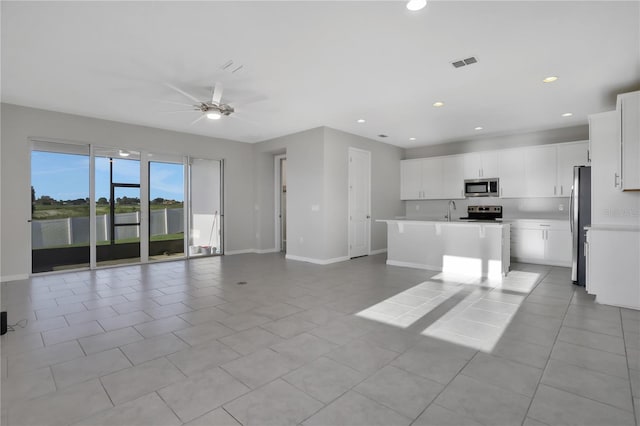 kitchen with appliances with stainless steel finishes, ceiling fan, sink, white cabinetry, and an island with sink