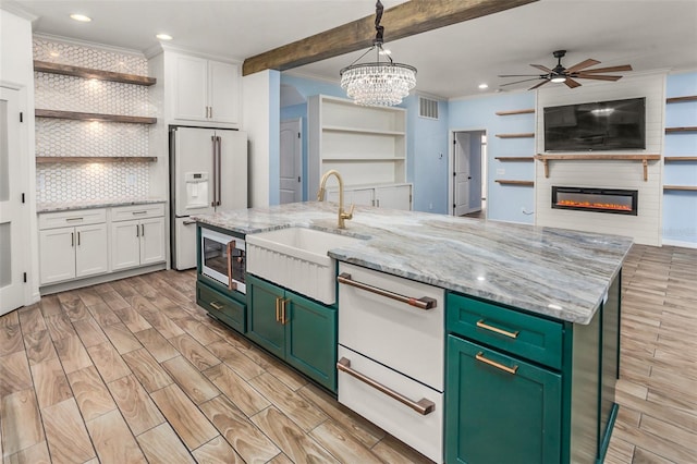 kitchen with white cabinetry, green cabinets, sink, and an island with sink