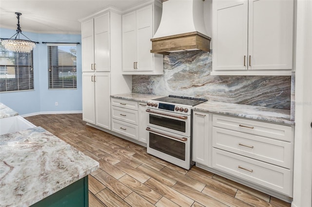 kitchen with range with two ovens, light wood-type flooring, white cabinetry, and premium range hood