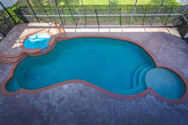 view of pool featuring an in ground hot tub, a patio area, and glass enclosure