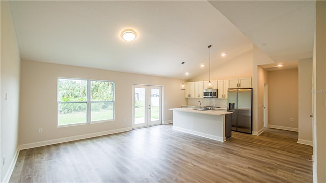 kitchen with light hardwood / wood-style flooring, decorative light fixtures, stainless steel appliances, a center island with sink, and white cabinets