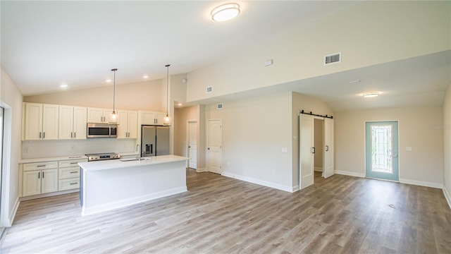 kitchen with white cabinets, a barn door, light wood-type flooring, stainless steel appliances, and an island with sink