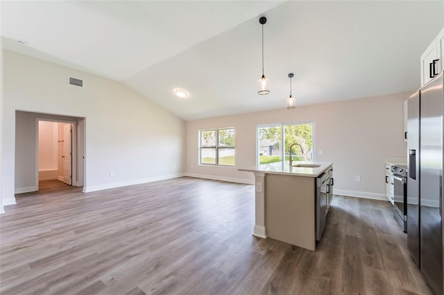 kitchen featuring decorative light fixtures, vaulted ceiling, dark hardwood / wood-style floors, an island with sink, and stainless steel appliances