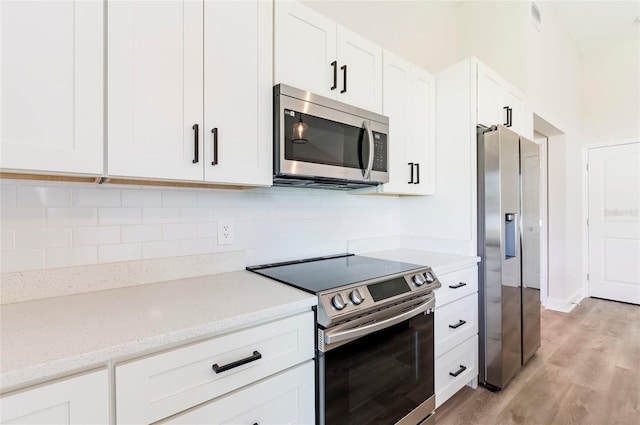 kitchen featuring white cabinetry, light hardwood / wood-style flooring, appliances with stainless steel finishes, light stone countertops, and decorative backsplash