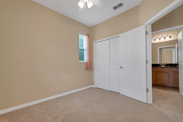 unfurnished bedroom with a closet, ceiling fan, light colored carpet, and ensuite bathroom