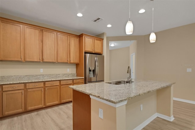 kitchen with sink, hanging light fixtures, light hardwood / wood-style flooring, a center island with sink, and stainless steel fridge