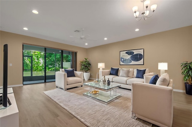 living room with ceiling fan with notable chandelier and light hardwood / wood-style flooring