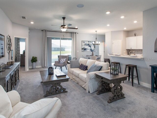 carpeted living room featuring sink and ceiling fan with notable chandelier