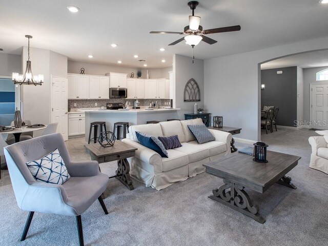 carpeted living room featuring ceiling fan with notable chandelier