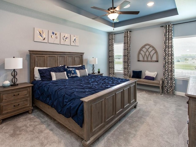 bedroom with multiple windows, light carpet, a tray ceiling, and ceiling fan