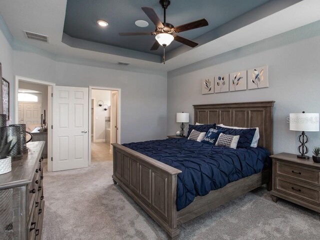 bedroom featuring ceiling fan, light carpet, ensuite bathroom, and a tray ceiling