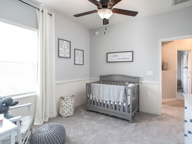 carpeted bedroom with ceiling fan, multiple windows, and a crib