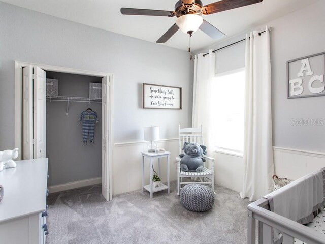 bedroom featuring a closet, ceiling fan, a crib, and light colored carpet