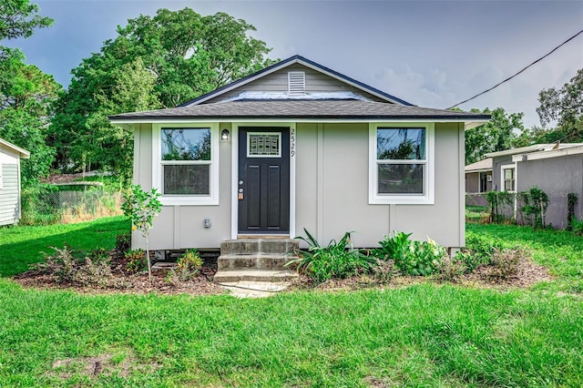 bungalow-style home with entry steps, a front lawn, roof with shingles, and fence