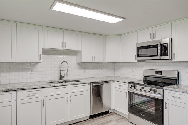 kitchen with light stone counters, stainless steel appliances, light wood-style flooring, white cabinetry, and a sink