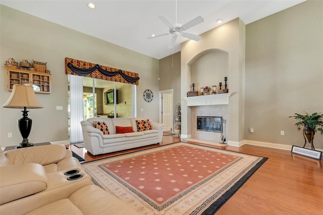 living room with a fireplace, ceiling fan, wood-type flooring, and a towering ceiling