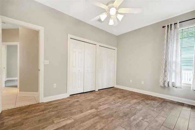 unfurnished bedroom featuring ceiling fan, two closets, and hardwood / wood-style floors