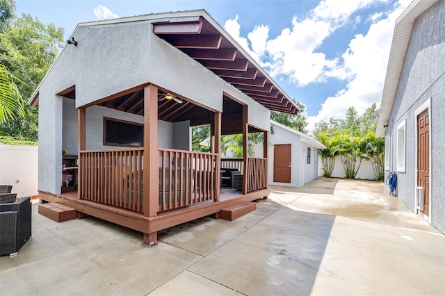 exterior space featuring stucco siding, a deck, a patio, fence, and an outdoor structure