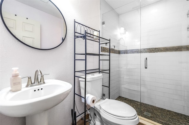 bathroom featuring a stall shower, toilet, a textured wall, and a sink