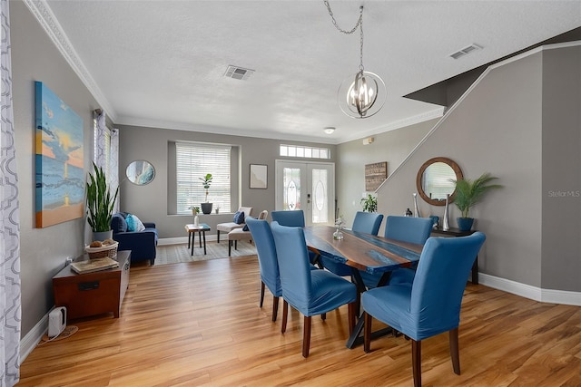 dining space featuring a chandelier, ornamental molding, a textured ceiling, and light wood-type flooring