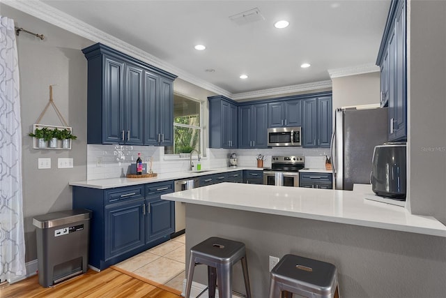 kitchen with appliances with stainless steel finishes, kitchen peninsula, a breakfast bar, sink, and blue cabinets