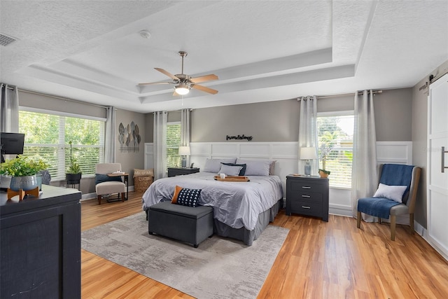 bedroom featuring ceiling fan, light hardwood / wood-style flooring, a barn door, and a raised ceiling