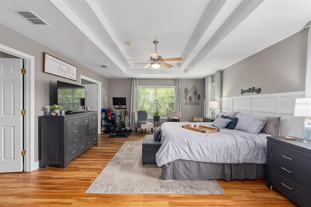 bedroom with a raised ceiling, ceiling fan, and light hardwood / wood-style flooring