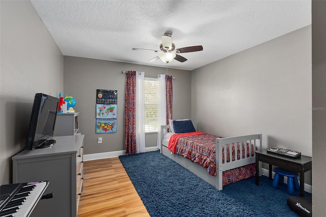 bedroom featuring ceiling fan, a textured ceiling, baseboards, and wood finished floors