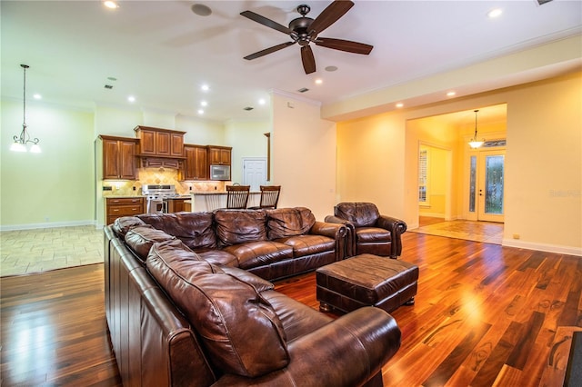 living room featuring dark wood-type flooring, ornamental molding, and ceiling fan with notable chandelier