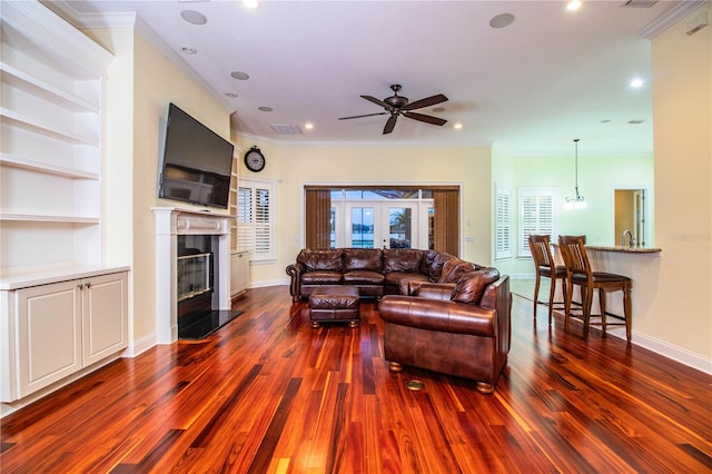 living room featuring built in shelves, ornamental molding, dark hardwood / wood-style flooring, ceiling fan, and french doors