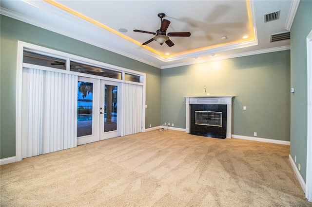 unfurnished living room featuring a fireplace, french doors, a tray ceiling, crown molding, and ceiling fan