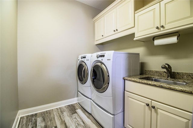 laundry area with light hardwood / wood-style flooring, cabinets, washer and dryer, and sink