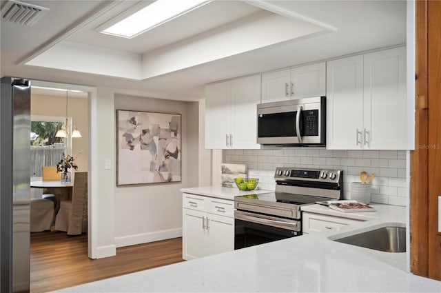 kitchen featuring decorative backsplash, appliances with stainless steel finishes, pendant lighting, white cabinets, and light hardwood / wood-style floors