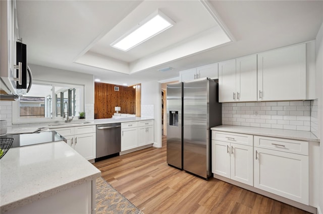 kitchen featuring light wood-type flooring, white cabinetry, appliances with stainless steel finishes, and a tray ceiling