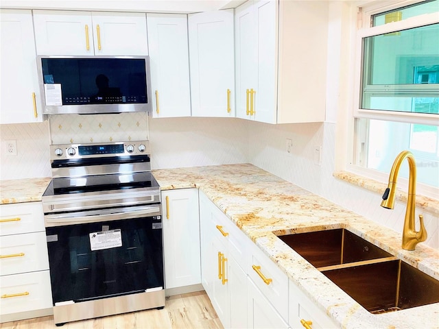 kitchen with sink, light stone counters, backsplash, stainless steel appliances, and white cabinets