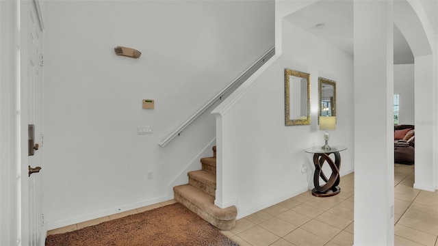 staircase with arched walkways, tile patterned flooring, and baseboards