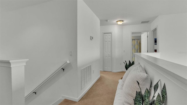 corridor with visible vents, baseboards, an upstairs landing, and light colored carpet