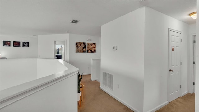 corridor with an upstairs landing, visible vents, and light colored carpet